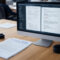 A photo of a business office with an open screen showing compliance monitoring software running. In the background, employees work normally. The focus is on a policy document titled “Employee Digital Use & Compliance” beside the monitor.